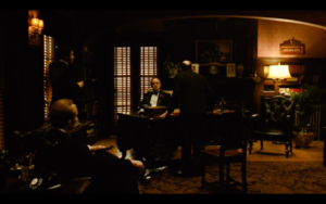In a dimly lit office, Vito Corleone (Marlon Brando) listens to the pleas of Bonasera (Salvatore Corsitto) to avenge his daughter, as Sonny Corleone (James Caan) and Tom Hagen (Robert Duvall) wait for Vito's orders.